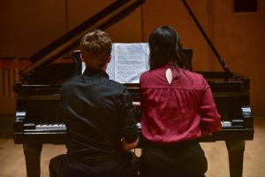 Young artists reading sheet music off of piano bench