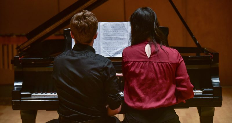 Young artists reading sheet music off of piano bench